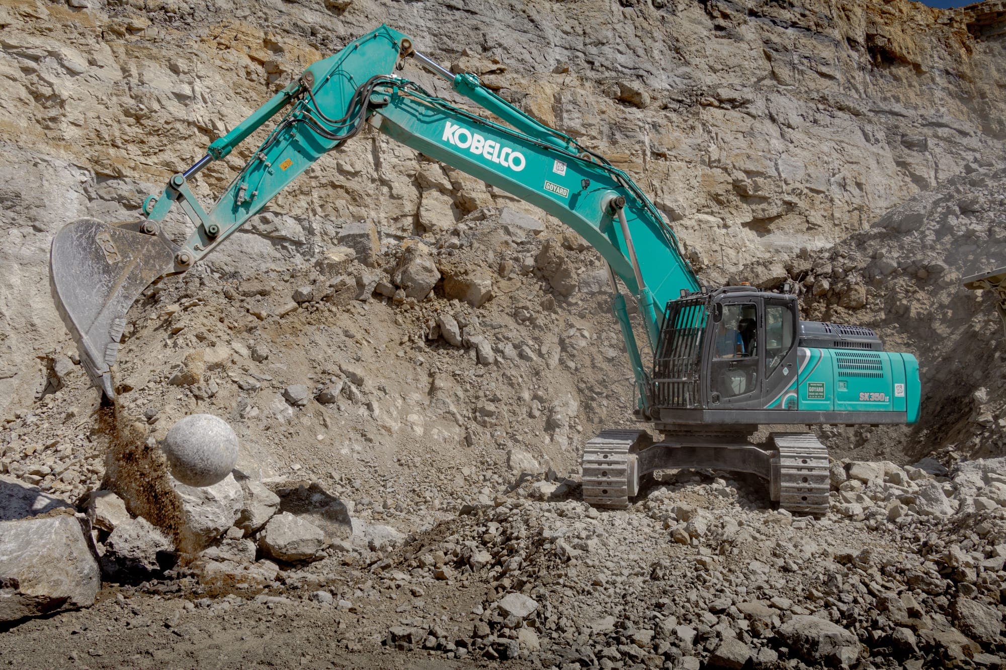Pelle hydraulique Kobelco vert d'eau extrayant des blocs au pied d'un front de taille, en carrière.